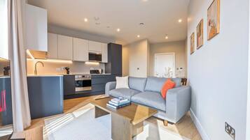 A modern living room with a grey sofa, a coffee table, and a kitchen in the background.