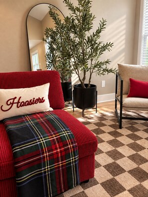 En rød sofa med et ternet pled, en pude med 'Hoasiers' broderet på, en potteplante og en stol med en rød pude.