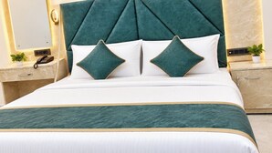 A bed with a tufted headboard, two pillows, a bedside table with a phone, and a nightstand with a plant. - The Rama Inn (Faizabad)