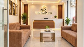 A reception area with a marble reception desk, two sofas, and a coffee table with a plant. - The Rama Inn (Faizabad)