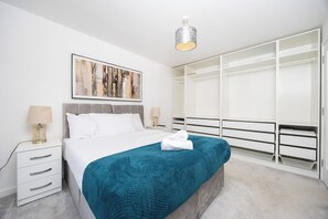 Quarto com cama, mesas de cabeceira, guarda-roupa e luminária no teto.