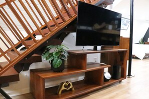 A staircase with a wooden railing, a black flat-screen TV mounted on a wooden stand, and a potted plant on the lower step. - Remote Work Ready Pond-view Hot Tub Home Gym (Savannah)