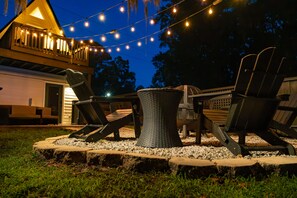 An outdoor seating area with chairs and a table, surrounded by a gravel border, under string lights.