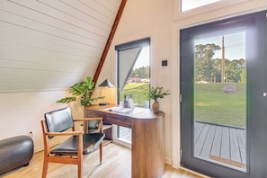 A modern room with a curved desk, a chair, a lamp, and a view of a grassy area through a large door.