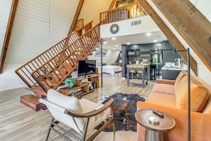 A loft-style living space with a wooden staircase, a kitchen area, a sofa, and a television.