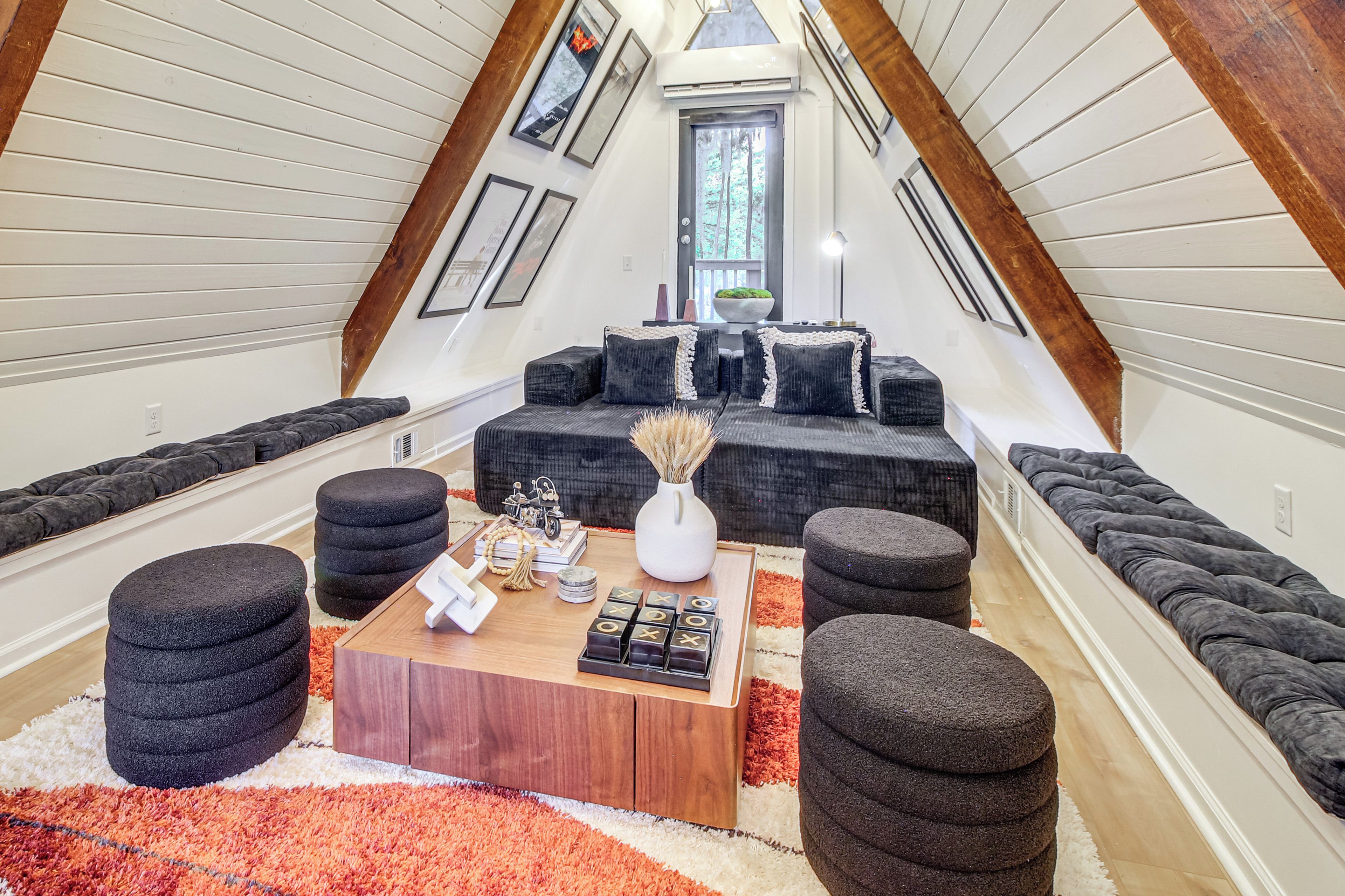 Un espacio tipo loft con techo de madera, un conjunto de sofás, otomanas, una mesa de centro y una alfombra.