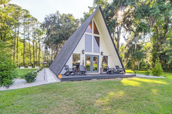 A modern A-frame house with a deck, outdoor seating, and a garden.