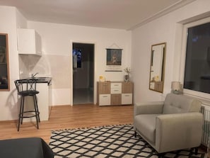 A compact living space with a kitchenette, a dining area, a sofa, and a large window. - Boutique Stay (Eberswalde)