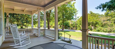 A covered porch with a rocking chair and a round table.