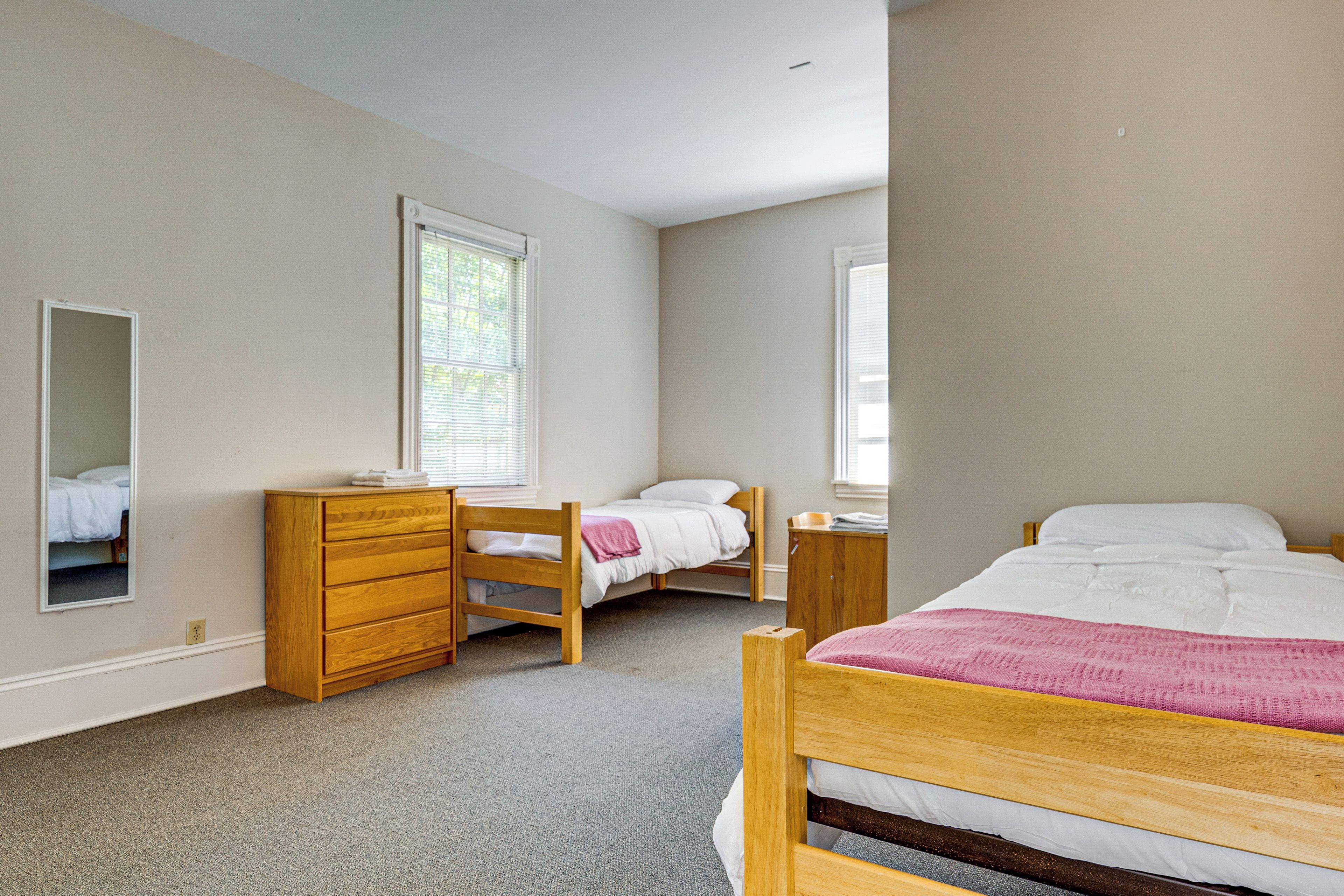 A bedroom with two beds, a dresser, and a mirror.