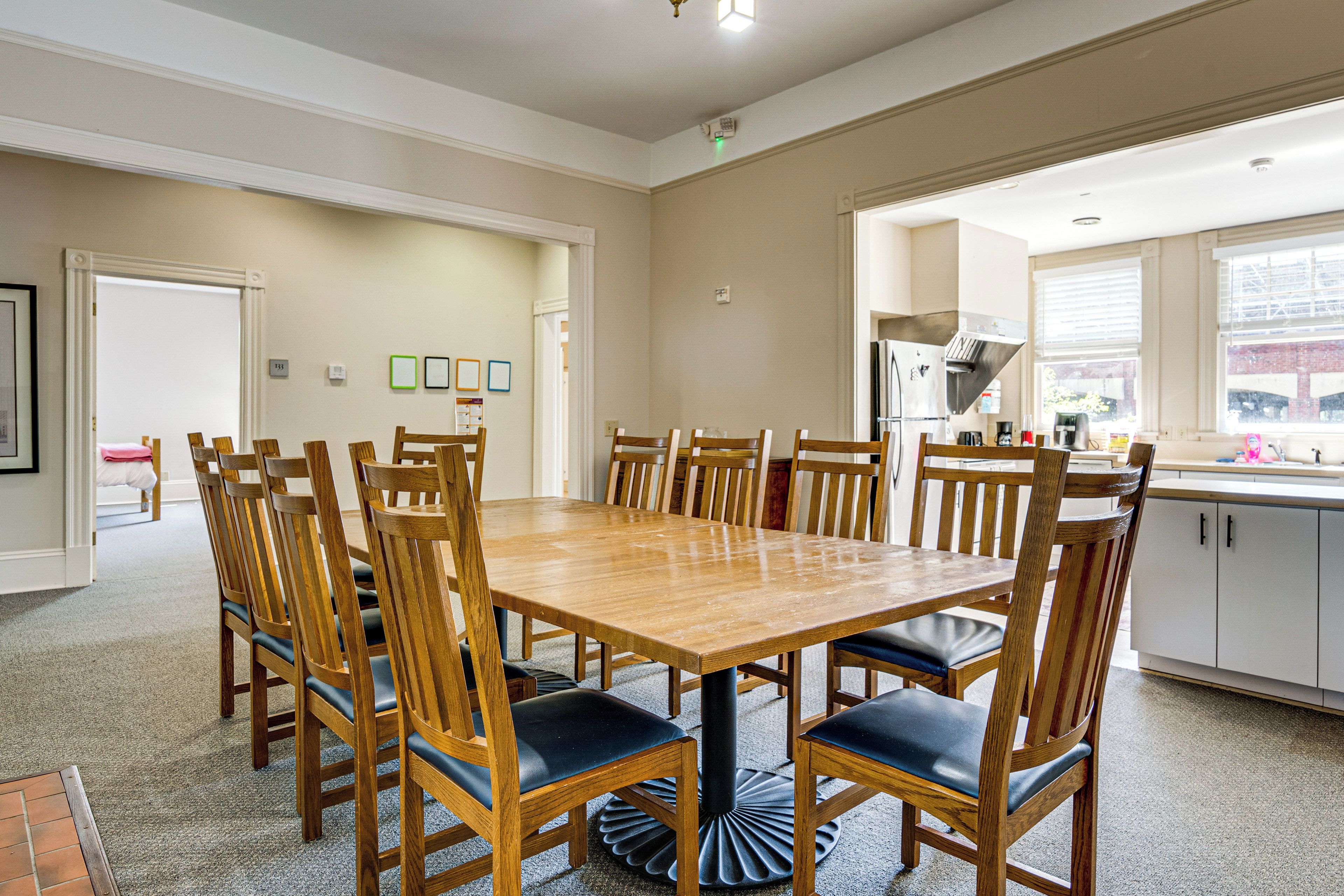 A dining area with a wooden table and chairs, a kitchen with a refrigerator and sink, and a window with blinds.