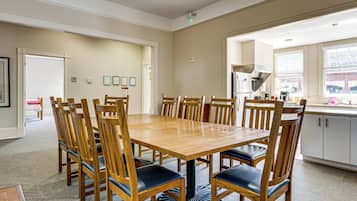 Un comedor con mesa y sillas de madera, una cocina con refrigerador y pileta, y un ventanal con persianas.