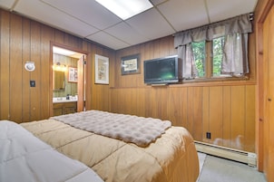 Una habitación con una cama, televisión, ventana con cortinas y paredes de madera.