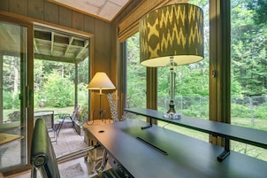 A room with a large window, a table with a lamp, and a chair.
