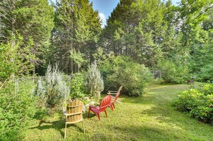 A fenced garden with a wooden chair and a red chair, surrounded by dense green foliage and trees.