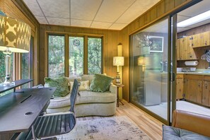 A cozy room with a sofa, a table, and a lamp. There is a window with a view of trees. - Patio, Sunroom! Forest Retreat Near North Conway (Conway)