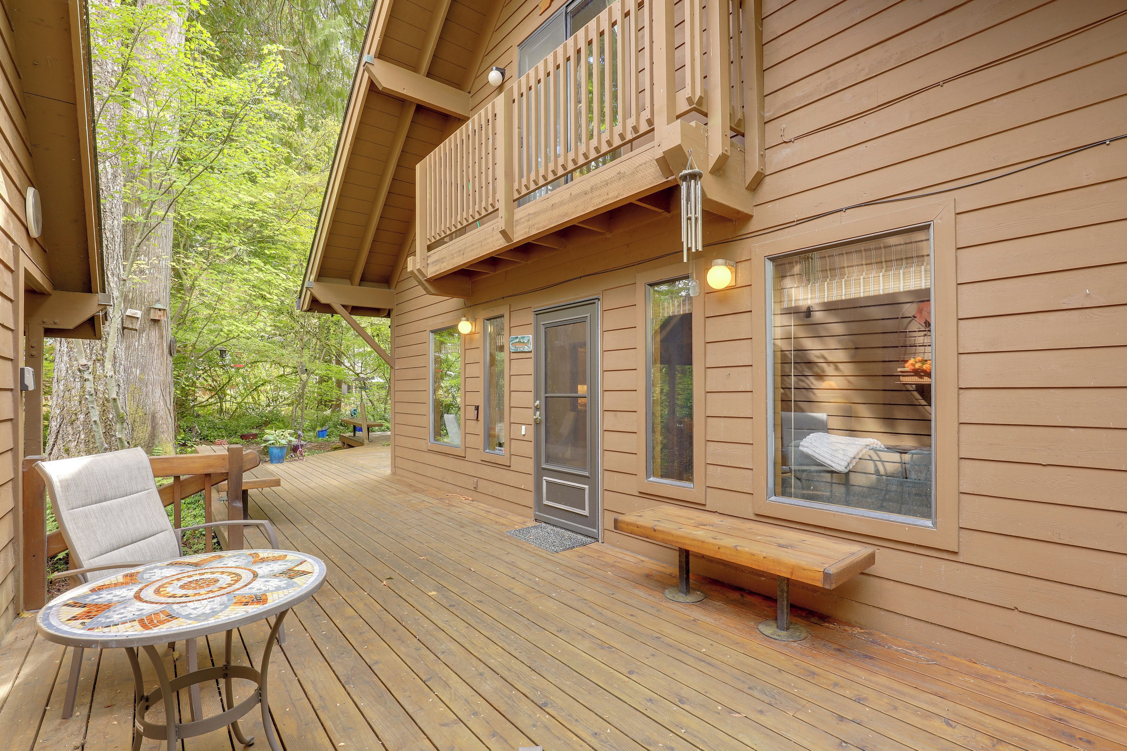 A wooden deck with a mosaic table, benches, and a door leading to a room with a window.