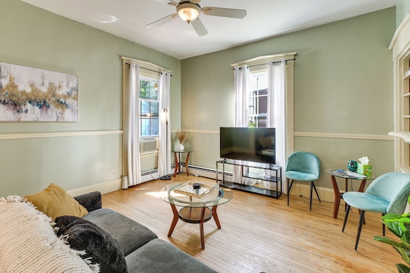 A living room with a grey sofa, a coffee table, a TV on a stand, and a ceiling fan.