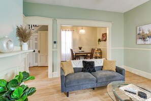 A living room with a grey sofa, a glass coffee table, and a dining area in the background.