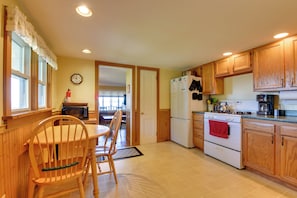 A kitchen with wooden cabinets, a stove, a refrigerator, and a dining table with chairs. - Fire Pit & Views! Lake Champlain Shoreline Stay (Plattsburgh)
