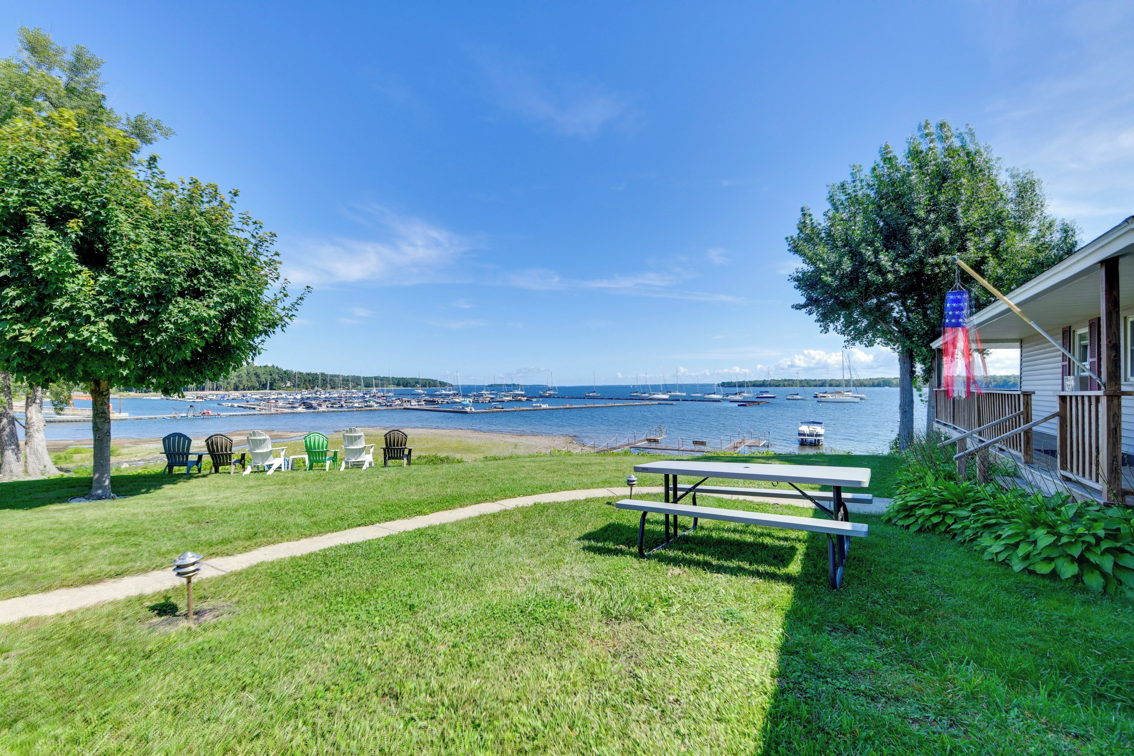 A grassy area with a picnic table and chairs, a dock with boats, and a clear view of the water.