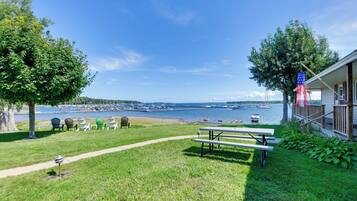 A grassy area with a picnic table and chairs, a dock with boats, and a clear view of the water.