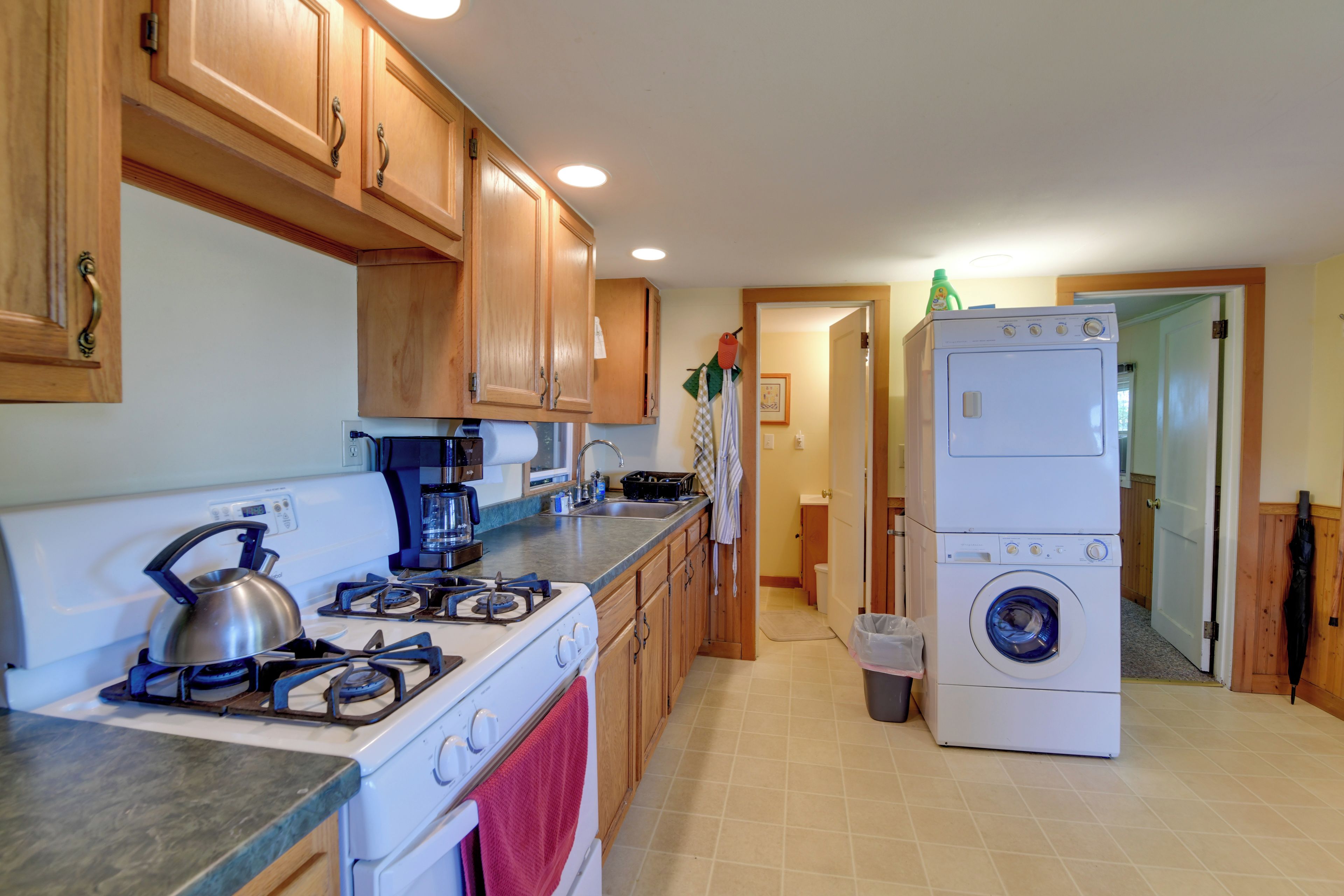 A kitchen with wooden cabinets, a gas stove, a coffee maker, and a stacked washer-dryer unit.