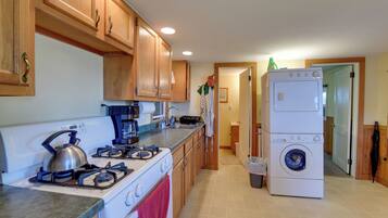 A kitchen with wooden cabinets, a gas stove, a coffee maker, and a stacked washer-dryer unit.
