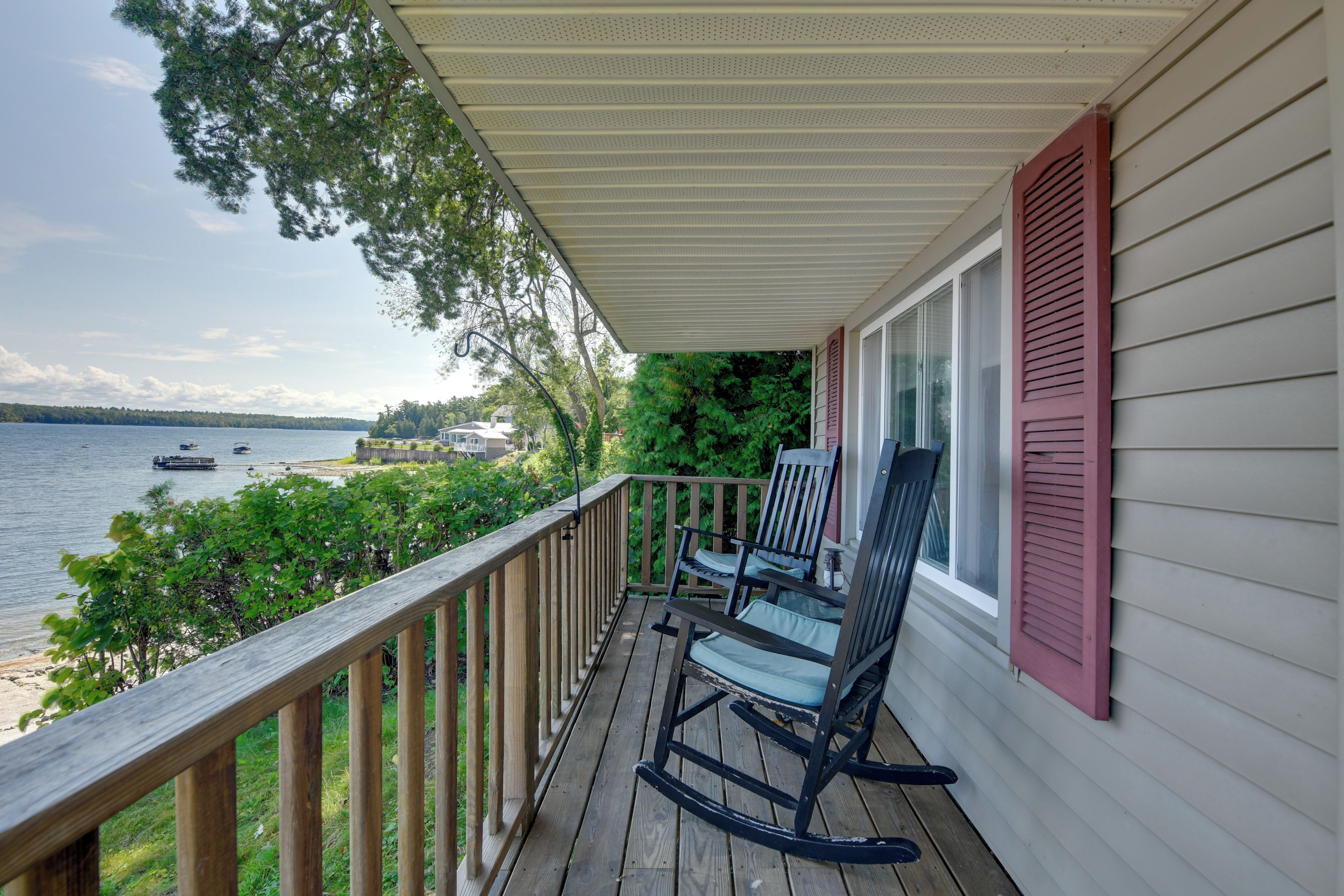A wooden deck with two rocking chairs, overlooking a lake with boats.