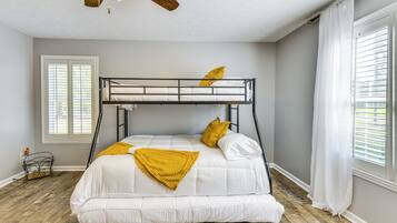 A bunk bed with white bedding and a yellow throw blanket, a ceiling fan, and a window with blinds.