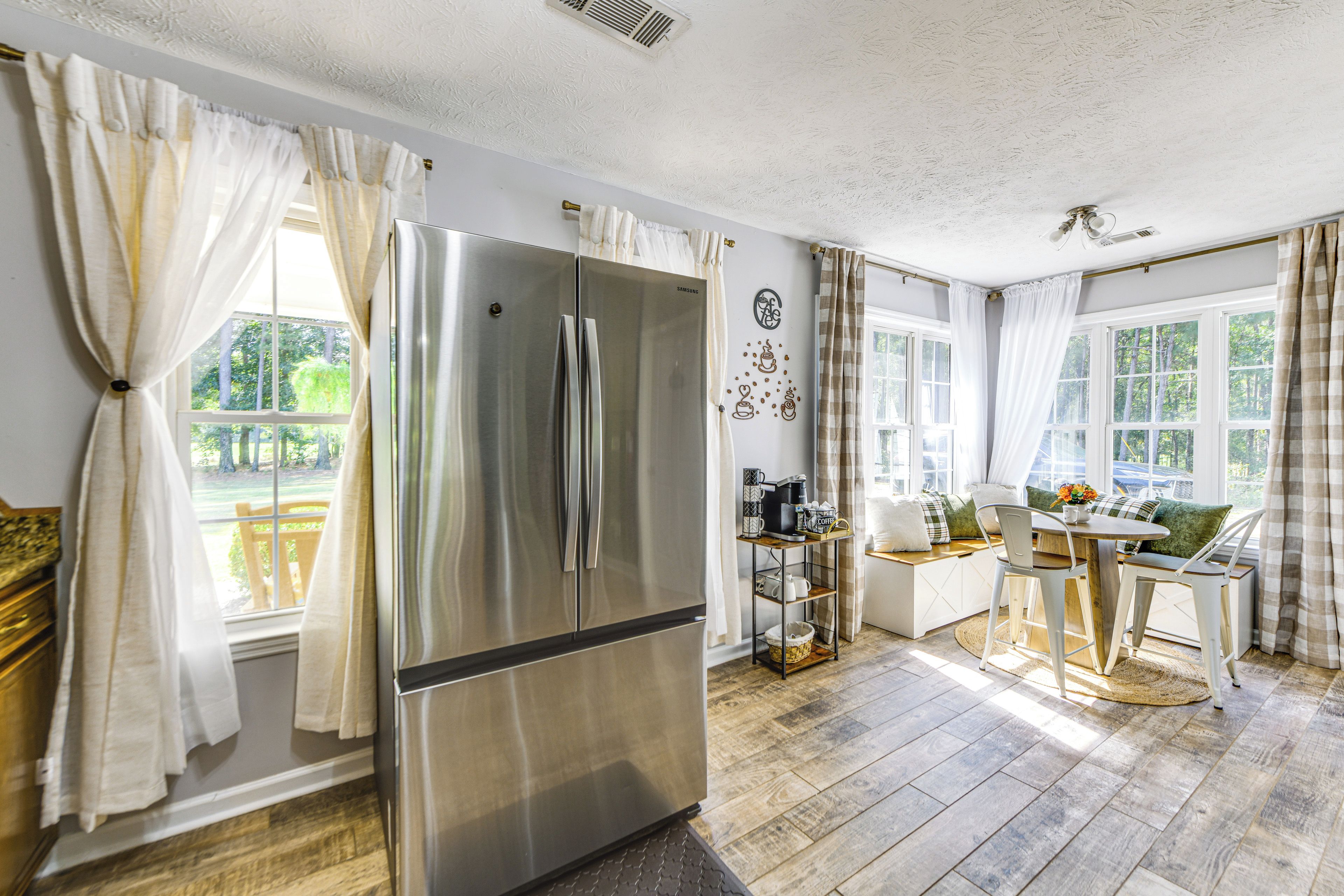 Una cocina moderna con un refrigerador de acero inoxidable, un comedor con mesa y sillas, y ventanas grandes con cortinas.