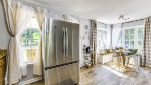 A modern kitchen with a stainless steel refrigerator, a dining area with a table and chairs, and large windows with curtains. - Game Day Hideaway! Spacious Opelika Escape (Opelika)