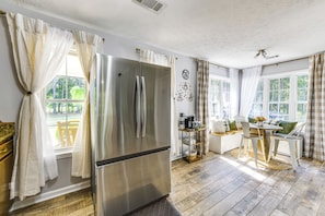Una cocina moderna con un refrigerador de acero inoxidable, un comedor con mesa y sillas, y ventanas grandes con cortinas.