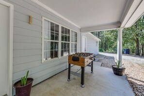 A covered outdoor area with a foosball table, a potted plant, and a house with windows and siding.