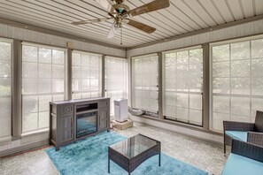 A sunroom with a ceiling fan, large windows, a fireplace, a glass coffee table, and wicker furniture. - Sun Porch w/ Fireplace! Family Home By Little Rock (Alexander)