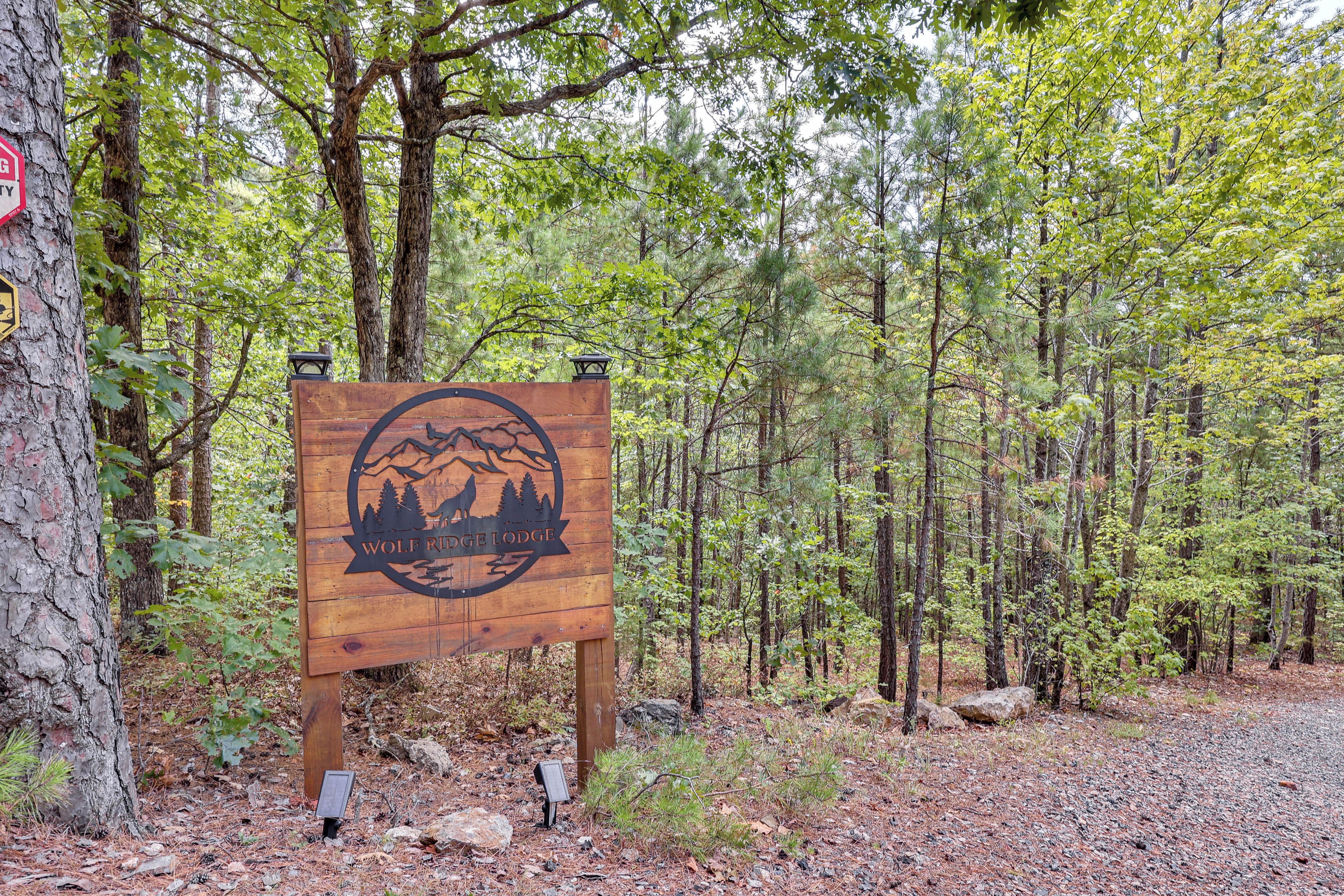 A wooden sign with a mountain and wolf silhouette, indicating a lodge named 'Wolf Ridge Lodge' in a forested area.