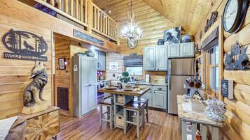 A cabin interior with a wooden interior, a dining area, kitchen, and a loft space.