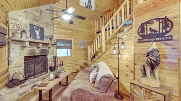 A cozy log cabin interior with a stone fireplace, a wooden staircase, and a welcome sign.