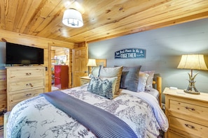 A cozy bedroom with a large bed, a television, wooden furniture, and a sign on the wall. - 'wolf Ridge Lodge' w/ Hot Tub & Fire Pit! (Mena)