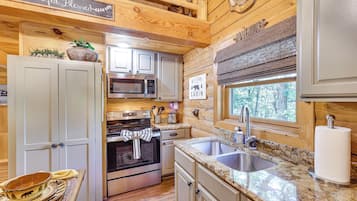 A cabin-style kitchen with wooden walls, a stainless steel oven, a microwave, and a sink.