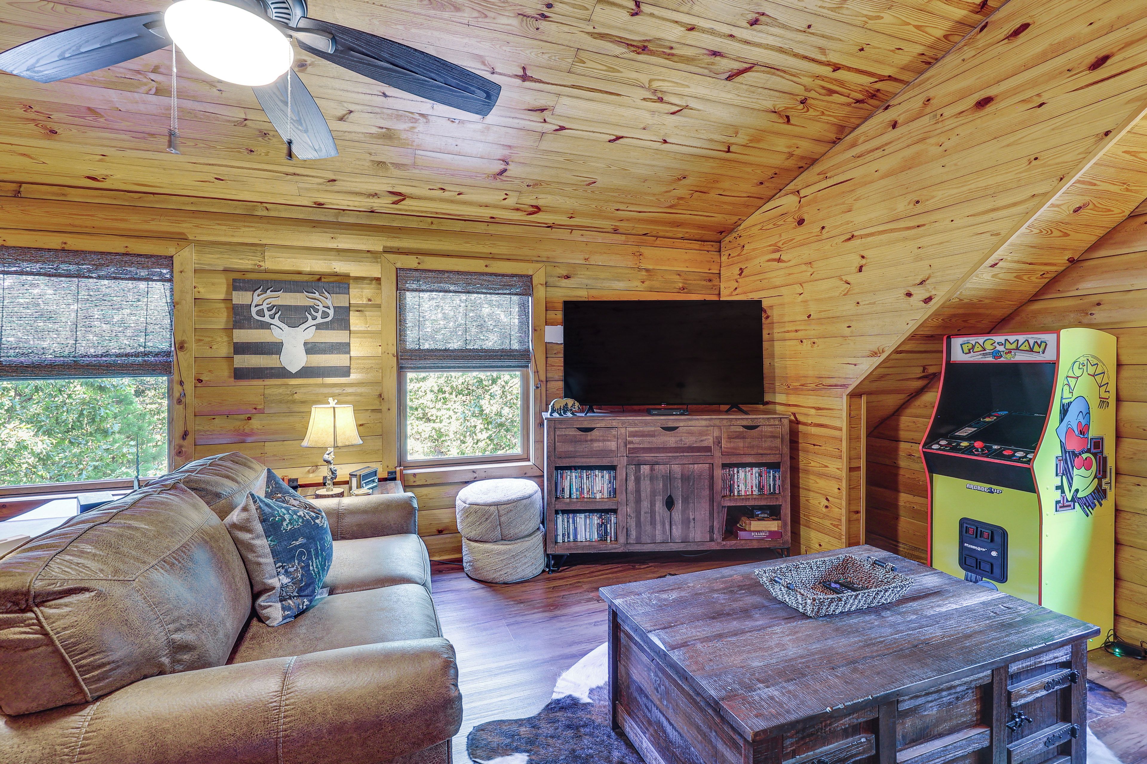 A cozy cabin interior with a ceiling fan, a television, a bookshelf, and a Pac-Man arcade machine.