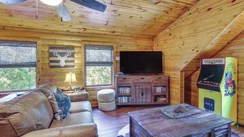 A cozy cabin interior with a ceiling fan, a television, a bookshelf, and a Pac-Man arcade machine.