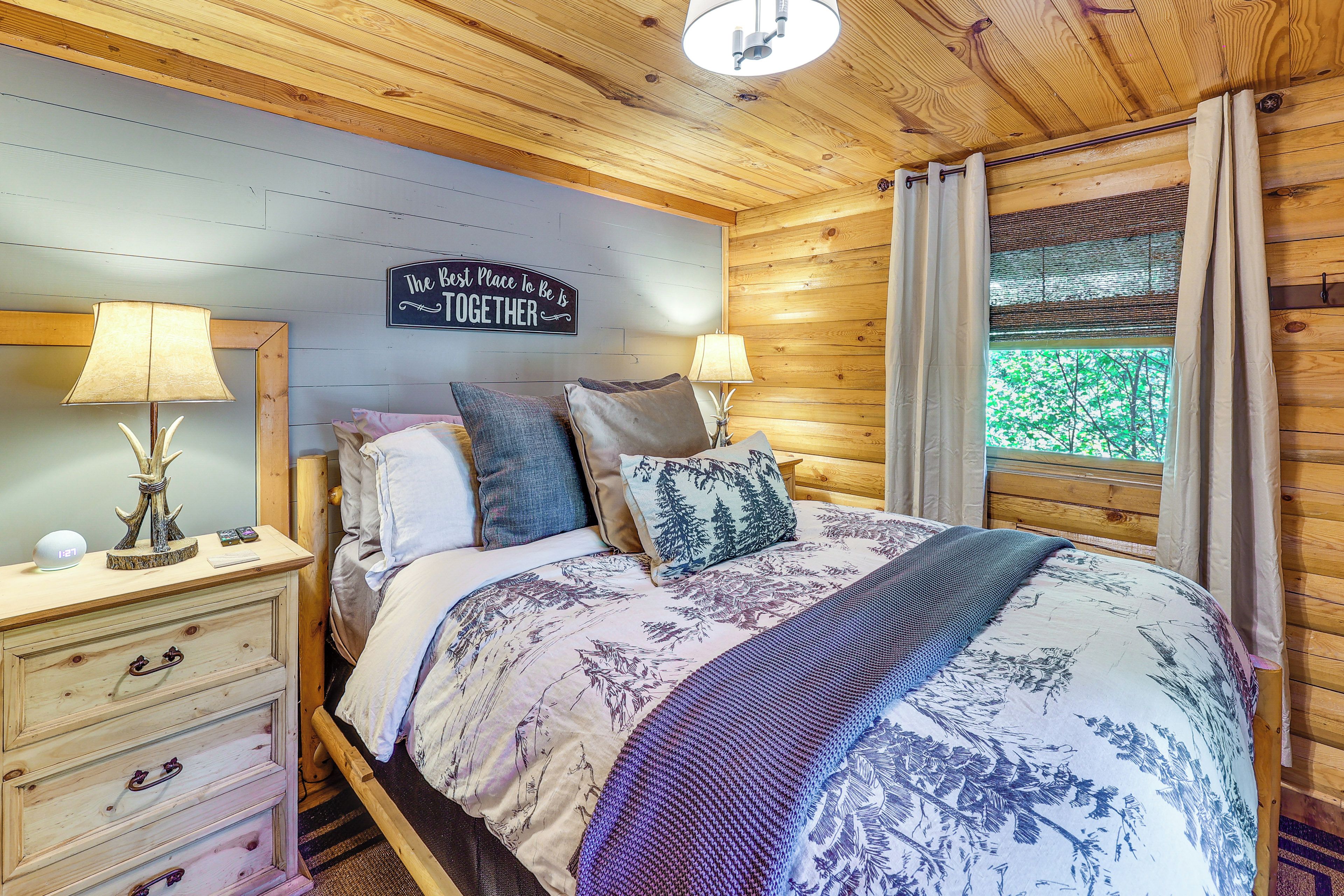 A cozy bedroom with a bed, two bedside tables, a wall clock, and a sign that reads 'The Best Place To Be Is Together.'