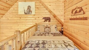 Un interno in legno con soffitto spiovente, un dipinto raffigurante una figura nativa americana, una silhouette di un orso e un attaccapanni.