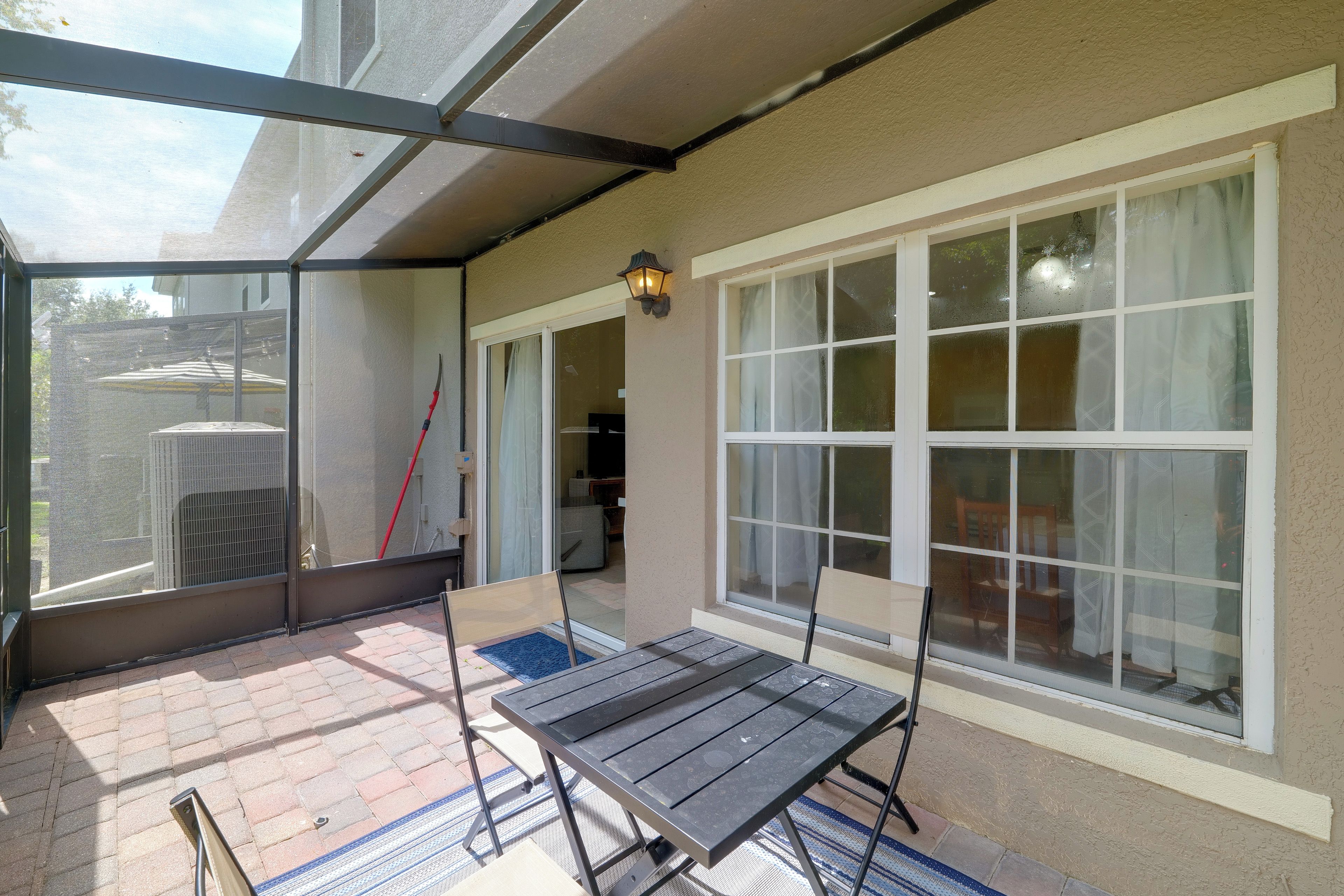 A covered patio with a table and chairs, large windows, and a view of the street.
