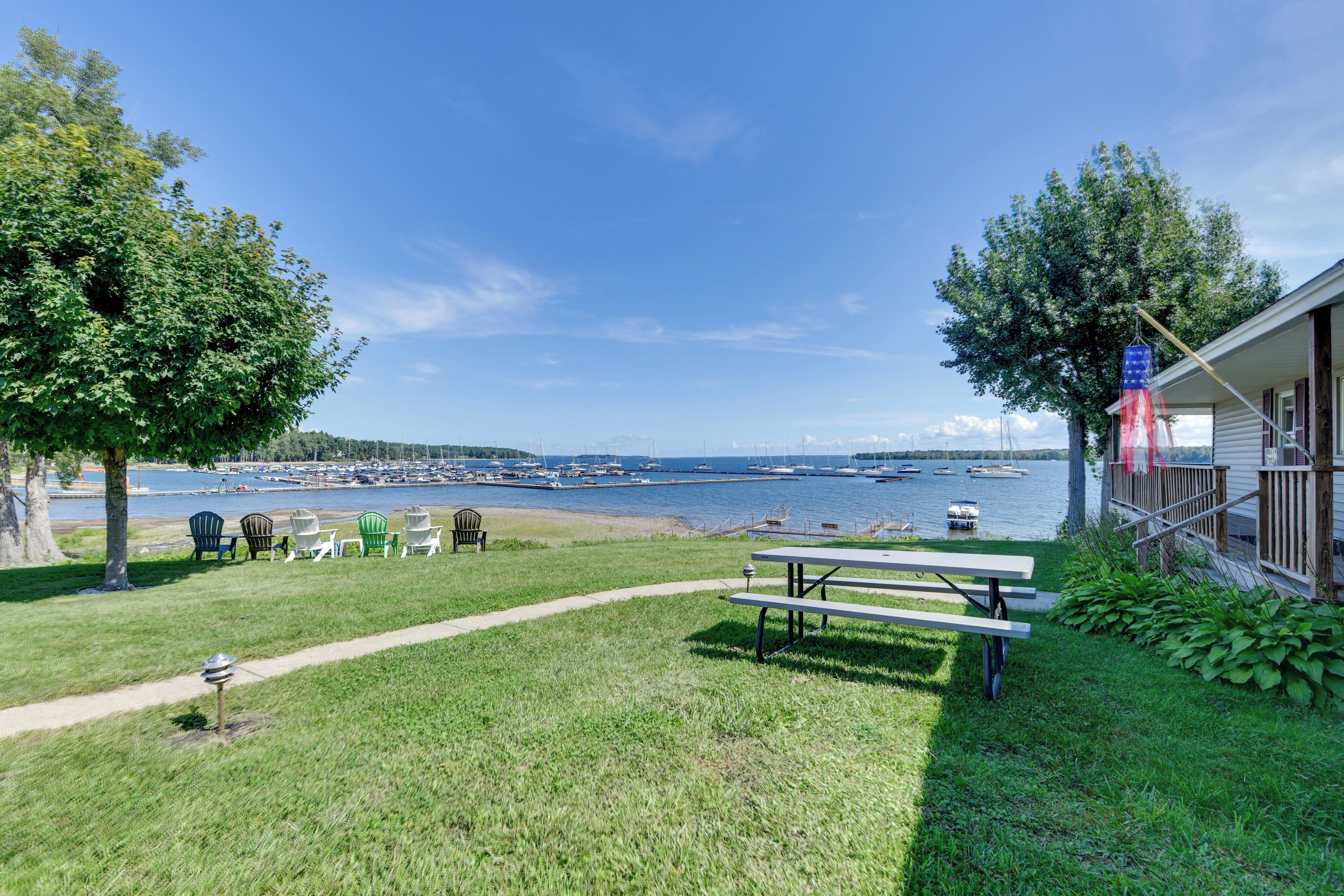 A grassy area with a picnic table and Adirondack chairs, overlooking a marina with boats.