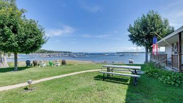 A grassy area with a picnic table and Adirondack chairs, overlooking a marina with boats.