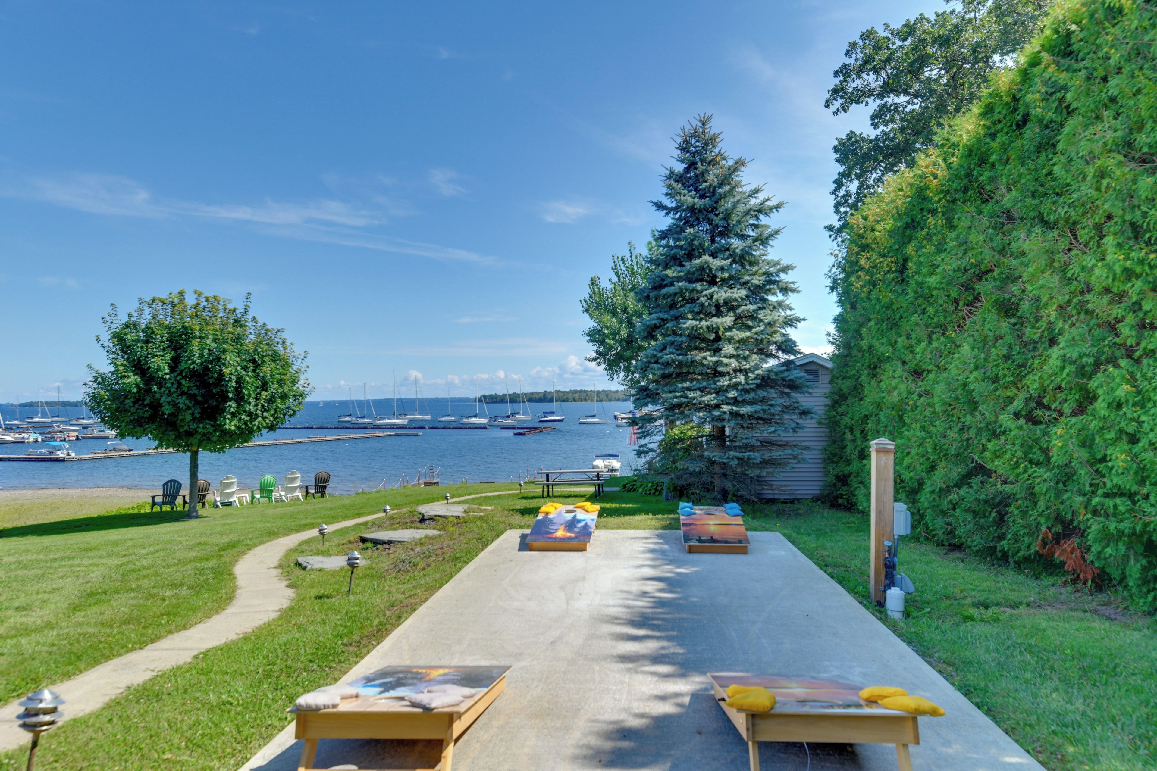 A waterfront property with a concrete pathway leading to outdoor seating, a large tree, and a view of boats on the water.