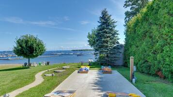 A waterfront property with a concrete pathway leading to outdoor seating, a large tree, and a view of boats on the water.