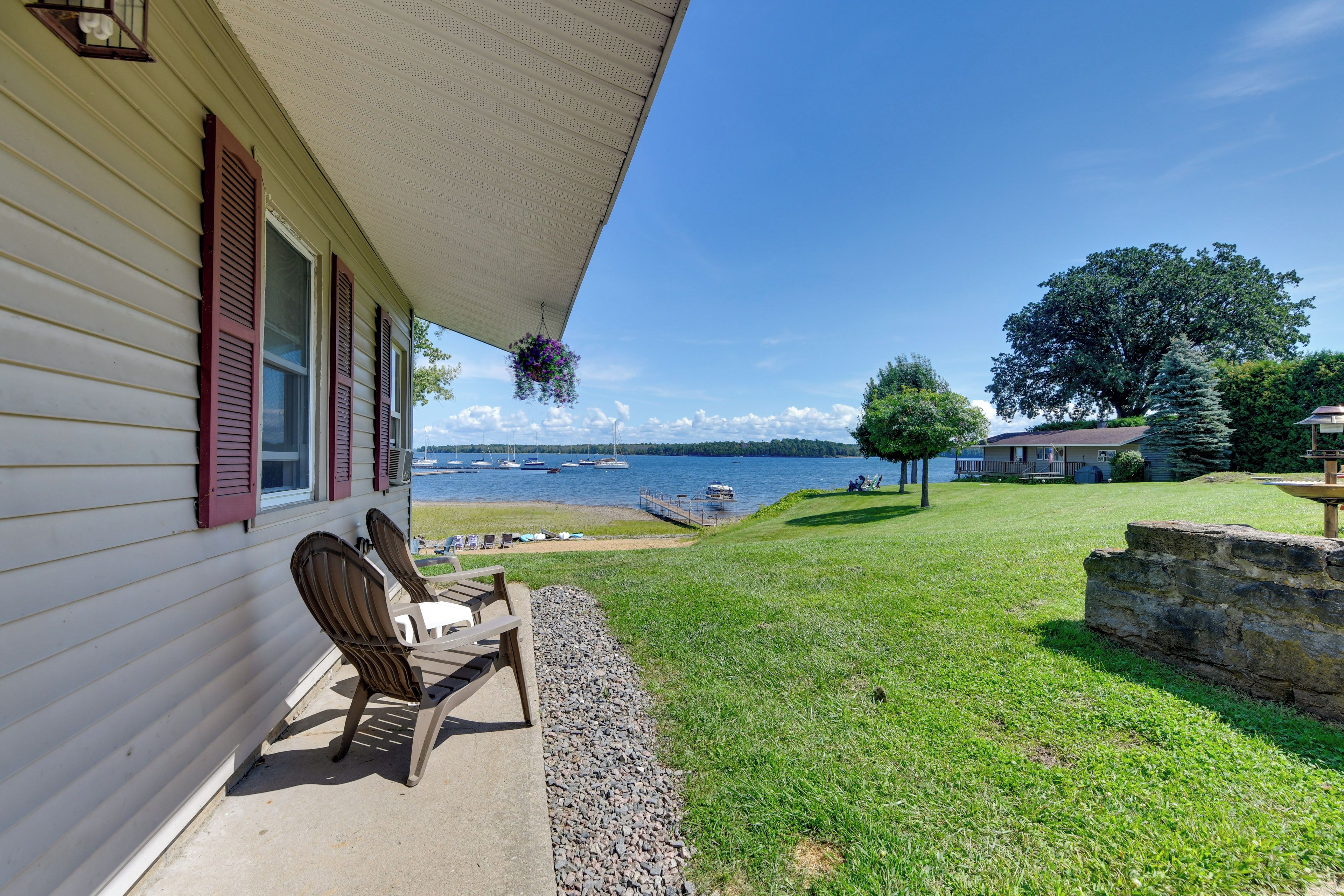 A house with a porch, a view of a lake with boats, and a stone wall.